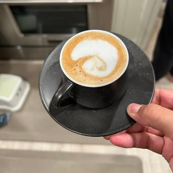 A latte in a black cup on a black saucer, leaf poured into the foam.