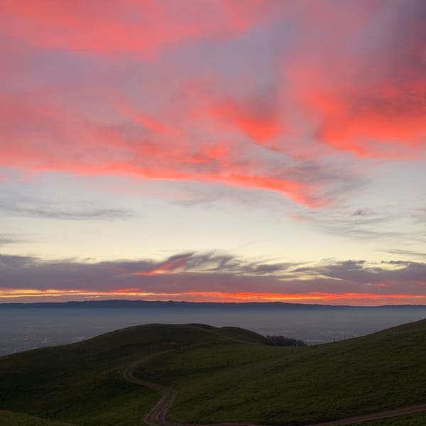 Pink cloud lit from below, over green hills at sunset.